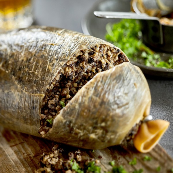 Traditional cooked Scottish haggis with chopped fresh herbs on a wooden hopping board cut through to show the texture of the meat